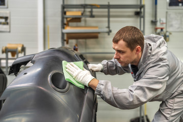 An employee of the paint shop of the automobile plant removes dust with a wax rag and prepares the bumpers for painting