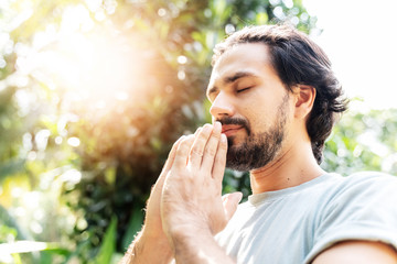 A bearded man is meditating outdoor in the park with face raised up to sky and eyes closed on sunny summer day. Concept of meditation, dreaming, wellbeing healthy lifestyle