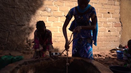 african teenage girl pulling up water with a rubber bucket at the village well