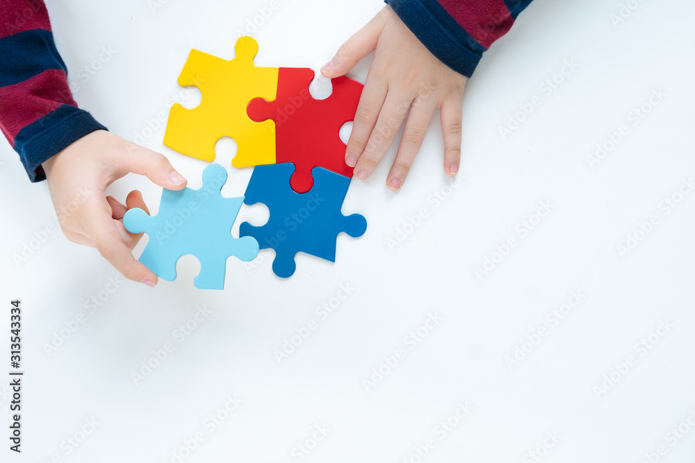Top view, hands of an autistic child play colorful puzzle which is a symbol of public awareness for autism spectrum disorder - World Autism Awareness day on April 2, Understanding and Acceptance. - obrazy, fototapety, plakaty 