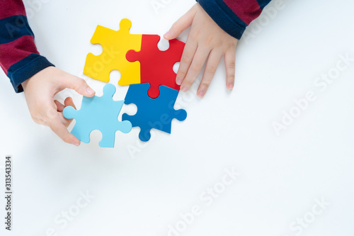 Top view, hands of an autistic child play colorful puzzle which is a symbol of public awareness for autism spectrum disorder - World Autism Awareness day on April 2, Understanding and Acceptance.