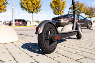 Close up view of e-scooter parked on sidewalk at cityscape on the sunset. Trendy urban transportation on modern electric scooter. Eco friendly mobility concept.