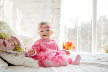 very nice charming little girl in pink dress laughs sitting on a bed