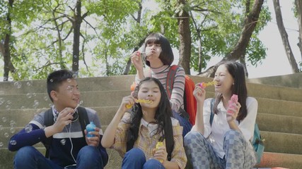 Wall Mural - Group of asian teenager blowing bubbles in park, slow motion shot.