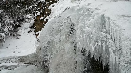 Wall Mural - frozen waterfall on a rock in the mountains. water flows from a frozen tonel.