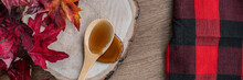 Maple Syrup Sweet Ingredient For Desssert Recipes, Liquid Dripping From Wooden Spoon On Wood Log Rustic Sugar Shack Banner Panoramic With Buffalo Plaid And Red Leaves.