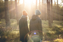 Couple In Warm Clothing Taking A Walk Inside A Sunny Forest