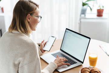 Canvas Print - Photo of happy caucasian woman typing on laptop and cellphone