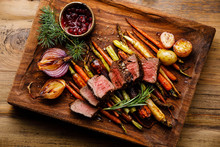 Grilled Sliced Venison Steak With Baked Vegetables And Berry Sauce On Wooden Background
