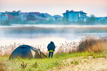 Canvas Print - Green tent and a man near river with morning mist on the water. Outdoor travel landscape