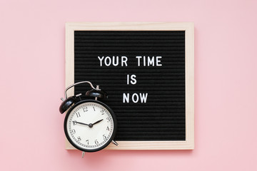 Wall Mural - Your time is now. Motivational quote on letter board and black alarm clock on pink background. Top view Flat lay Concept inspirational quote of the day.