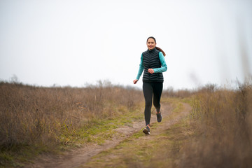 Beautiful Smiling Woman Running on the Mountain Trail at Cold Autumn Evening. Sport and Active Lifestyle.