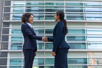 Happy business ladies meeting near office building. Business women shaking hands with each other outside in city. Congratulation concept