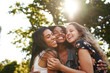 Portrait of a happy multiethnic group female friends hugging and embracing each other laughing and having fun outdoors in a park 