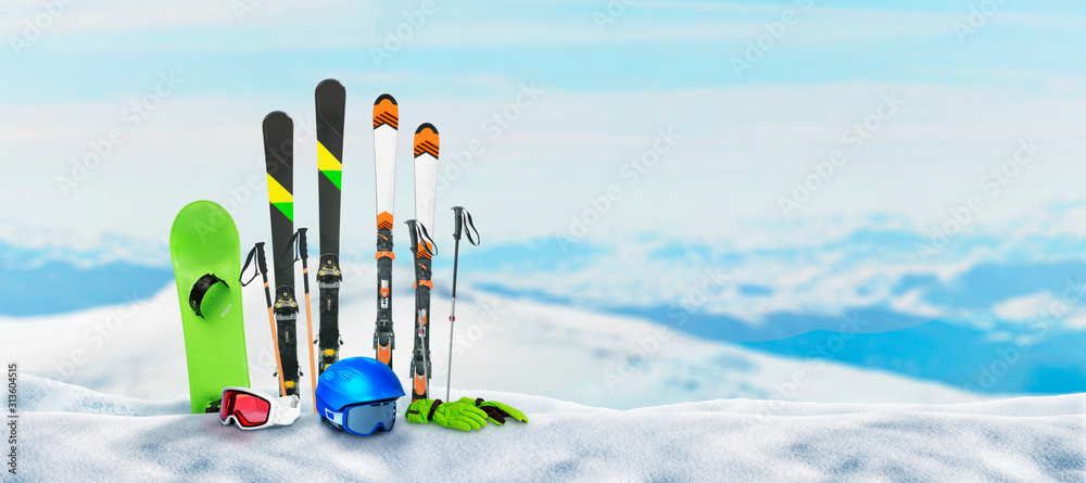 Ski equipment pinned to the snow on top of a mountain. Concept of winter holidays and snow sports. Snowy mountain peaks in the background - obrazy, fototapety, plakaty 