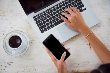 Business woman hand holding mobile phone blank screen with clipping path using laptop computer and drinking coffee while working on office table.