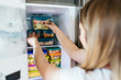 © hedgehog94 - Woman placing container with frozen mixed vegetables in freezer.