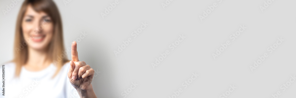 Young woman touches or pushes a finger at something on a light background. Banner - obrazy, fototapety, plakaty 