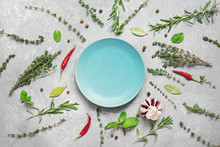 Empty Blue Plate And Frame Of Herbs And Spices On A Gray Concrete Background. Thyme, Rosemary, Bay Leaf, Peppercorns, Garlic, Mint And Chili Peppers. Top View, Flat Lay.