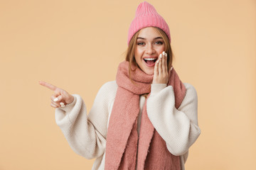 Wall Mural - Image of young girl in winter hat smiling and pointing finger aside