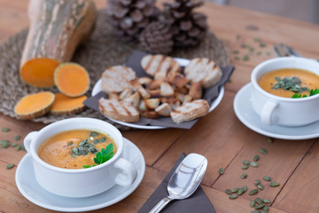 A raw pumpink in the middle of the table. Healthy eating in autumn and winter time. Wooden table with two bowls of pumpkin cream soup.