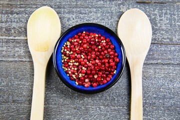 Closeup view from above on blue bowl with red pepper corns, two spoons on wood table