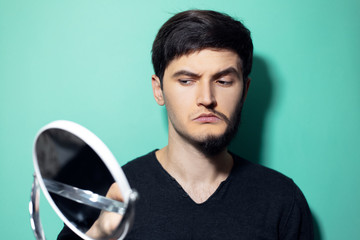 Wall Mural - Studio portrait of young surprised man with half shaved face, looking in mirror  on background of aqua menthe color.