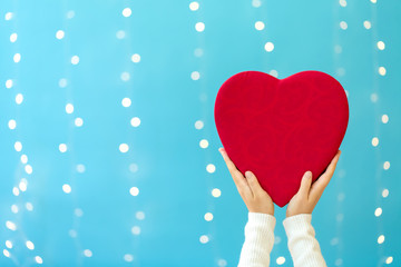 Canvas Print - Young woman holding a big Valentine's day heart on a shiny light blue background