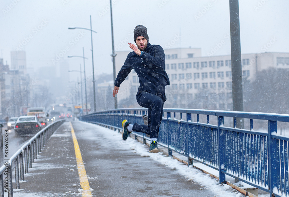 Young man running in city street at cold winter day. - obrazy, fototapety, plakaty 