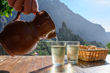 Man Pouring White Wine From Clay Jug Into Glass On Terrace With View On Green Landscapes Of Small Mountain Village Masca On Tenerife, Spain