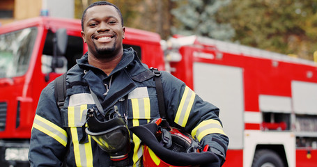 Firefighter portrait on duty. Photo of happy fireman with gas mask and helmet near fire engine