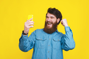 Happy young trendy man looking at smartphone and celebrating