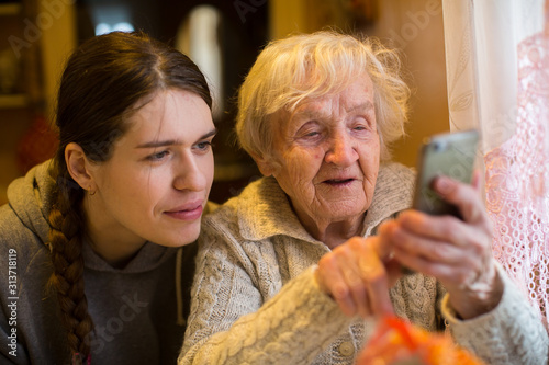 Fotomural An elderly old woman looks at a smartphone his adult granddaughter