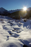 Fototapeta  - Winter hiking in Aosta Valley, Cogne, Italy. The sun is setting behind the mountains.  Backlit shot with the sun inside the frame.