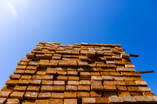A Bright Sunny Glare Is View From Below, Shining Over A Large Pile Of Treated Wood Planks, 4 By 2 Boards Used In Construction Of Stud Walls, With Copy Space