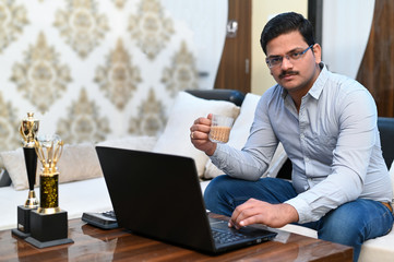 Young successful businessman working on laptop and filling tea cup with tea for refreshment after too much work.