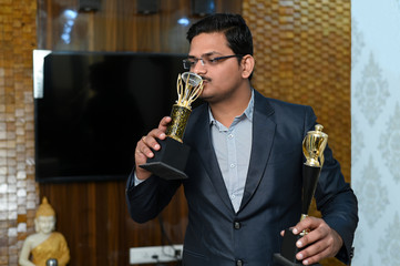 young successful asian / indian businessman showing trophy after winning awards