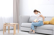 © New Africa - Young woman suffering from hemorrhoid on sofa at home