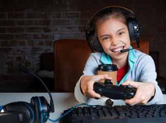 A young girl is sitting in front of a monitor and playing video games with a happy excited face.