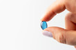 © TATIANA KIM - Female hand holds blue capsule isolated on white background.