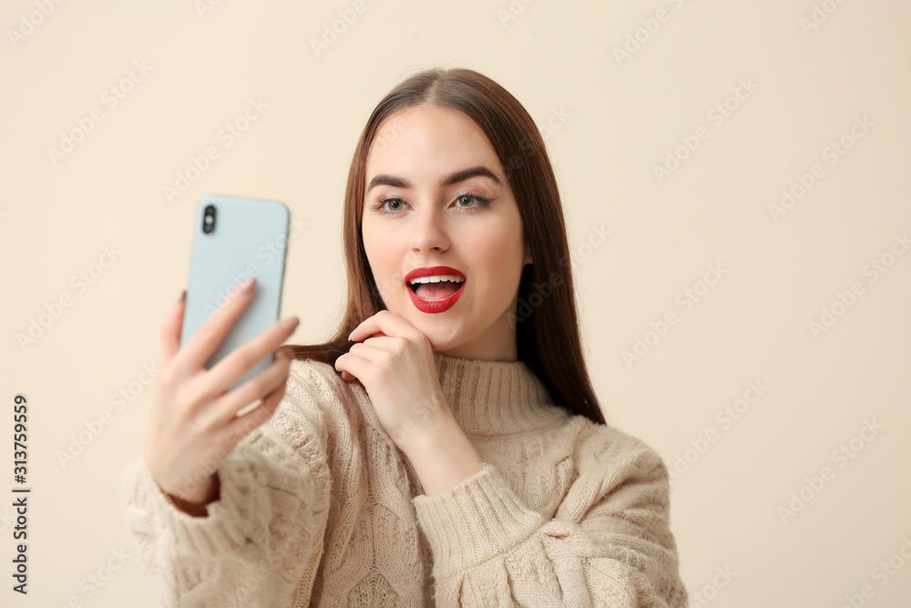 Beautiful young woman taking selfie on light background