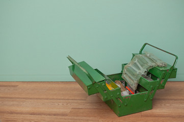 Green metal toolbox on a wooden floor with a green background. Closeup photo with copyspace.