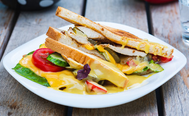 Classic breakfast, hot sandwiches with cheese, vegetables and chicken on a wooden table.