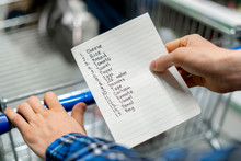 Person's Hands Holding A Shopping List Paper Sheet And Check Buying Products In Grocery Store