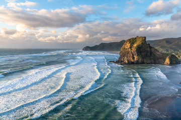 View of long surfing waves with white foam at Piha beach