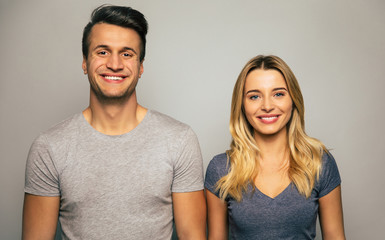 Simple looks. Close-up photo of a beautiful couple, who are posing in grey t-shirts, standing with their arms down, looking in the camera and smiling.