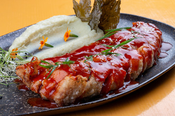 Carp in sweet and sour Chinese sauce with mashed potatoes and grape leaves. On a dark ceramic platter.