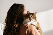 © Evrymmnt - Portrait of young woman holding cute siberian cat with green eyes. Female hugging her cute long hair kitty. Background, copy space, close up. Adorable domestic pet concept.