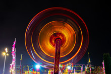 Photo Of A Carousel At Night In A Long Exposure In An Amusement Park. The Yellow And Redder Tones Of The Carousel Bulbs Merge In Motion And Give The Image A Glowing Disk Effect.