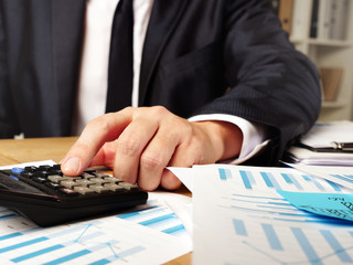 Wall Mural - Man is calculating annual financial report with calculator and stack of paper.